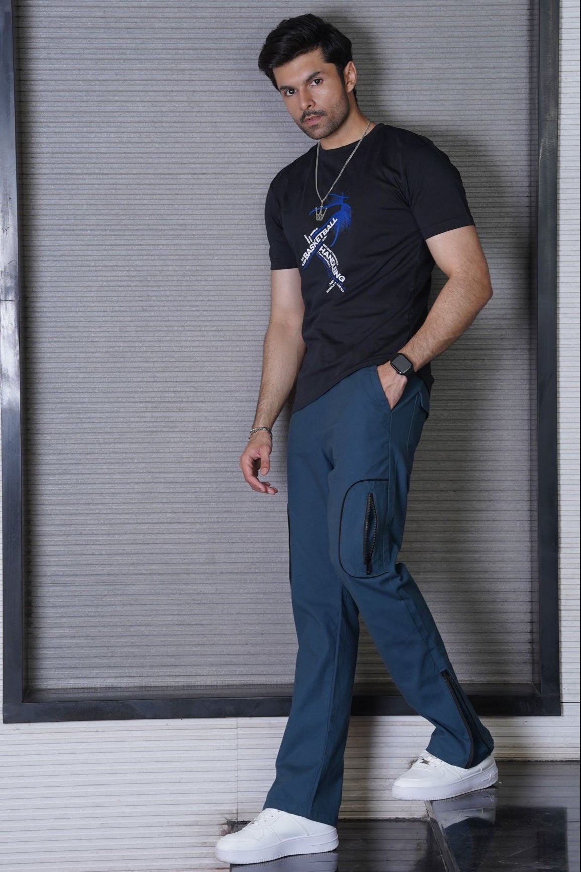 Man wearing a black t-shirt with a graphic design and blue pants against a gray wall.