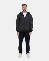 Man wearing a dark gray hoodie and black pants on a light blue background