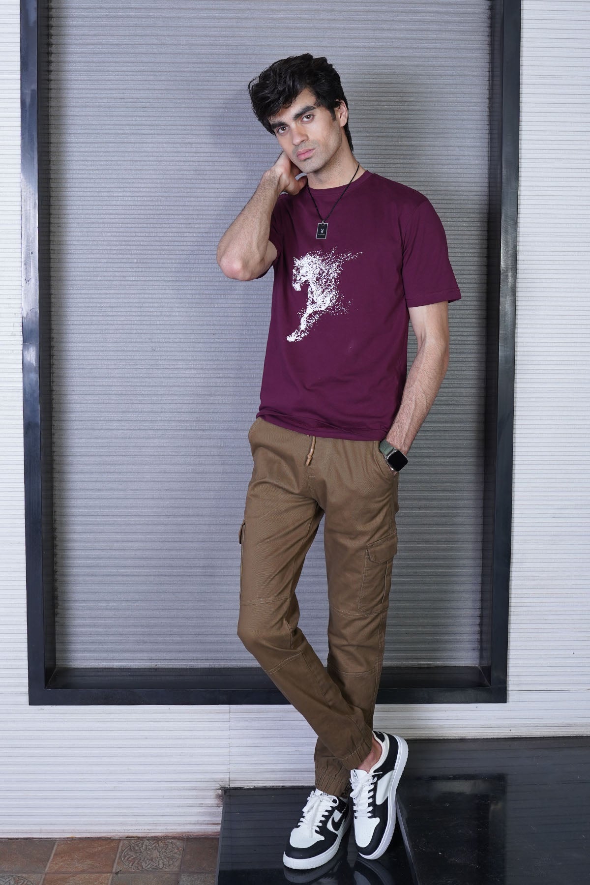 A person wearing a maroon graphic t-shirt with a horse design, paired with brown trousers and white sneakers.
