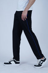 A man wearing black track pants with blue stitching and a white t-shirt, standing against a blue background.