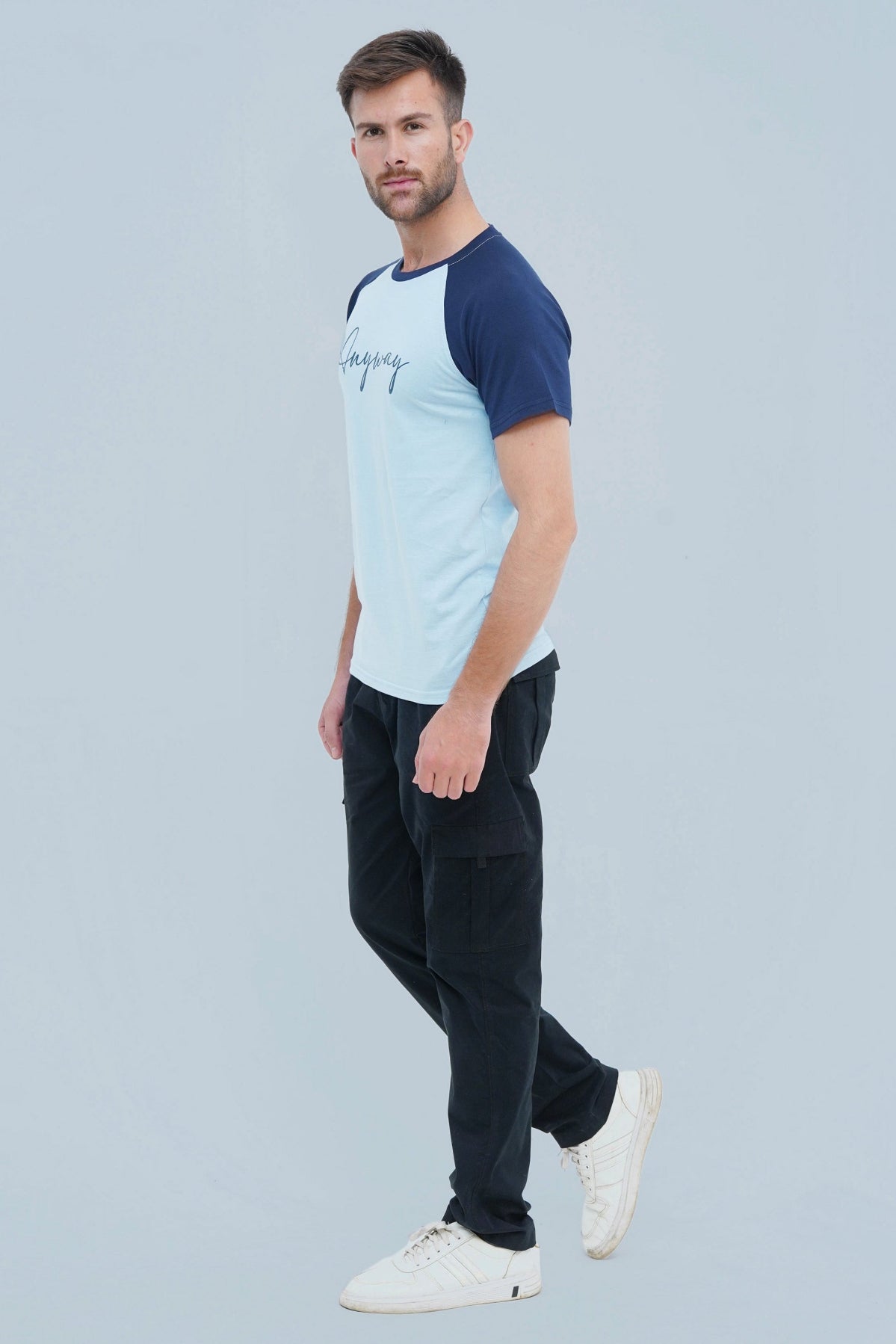 A male model wearing a blue t-shirt with text on the front and contrasting sleeves, paired with black pants and white sneakers.