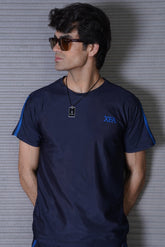 A person wearing a navy t-shirt with contrast stripes, standing against a striped background.