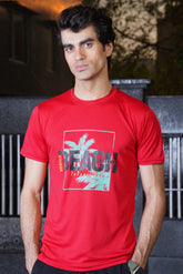 A male model wearing a red Venice Beach graphic T-shirt with a palm tree and text design on the front.