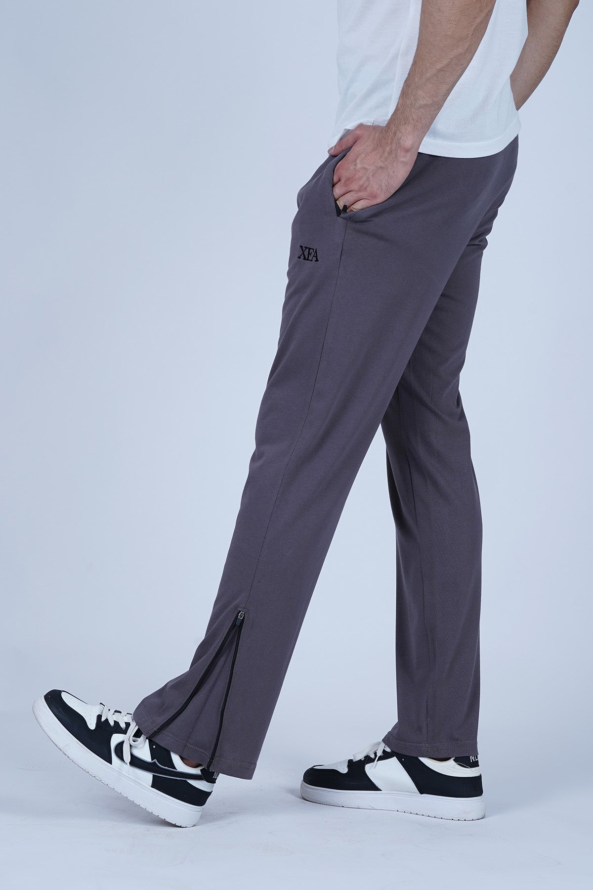 A man wearing grey track pants with side zip pockets and a zip hem, paired with a white t-shirt and black sneakers.