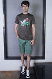 Man wearing a gray t-shirt with colorful graphics and green shorts standing in front of a window.