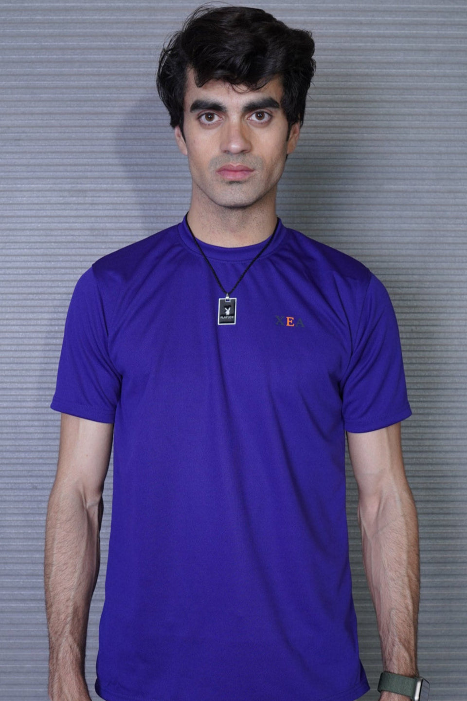 Man wearing a purple shirt with a logo against a gray background