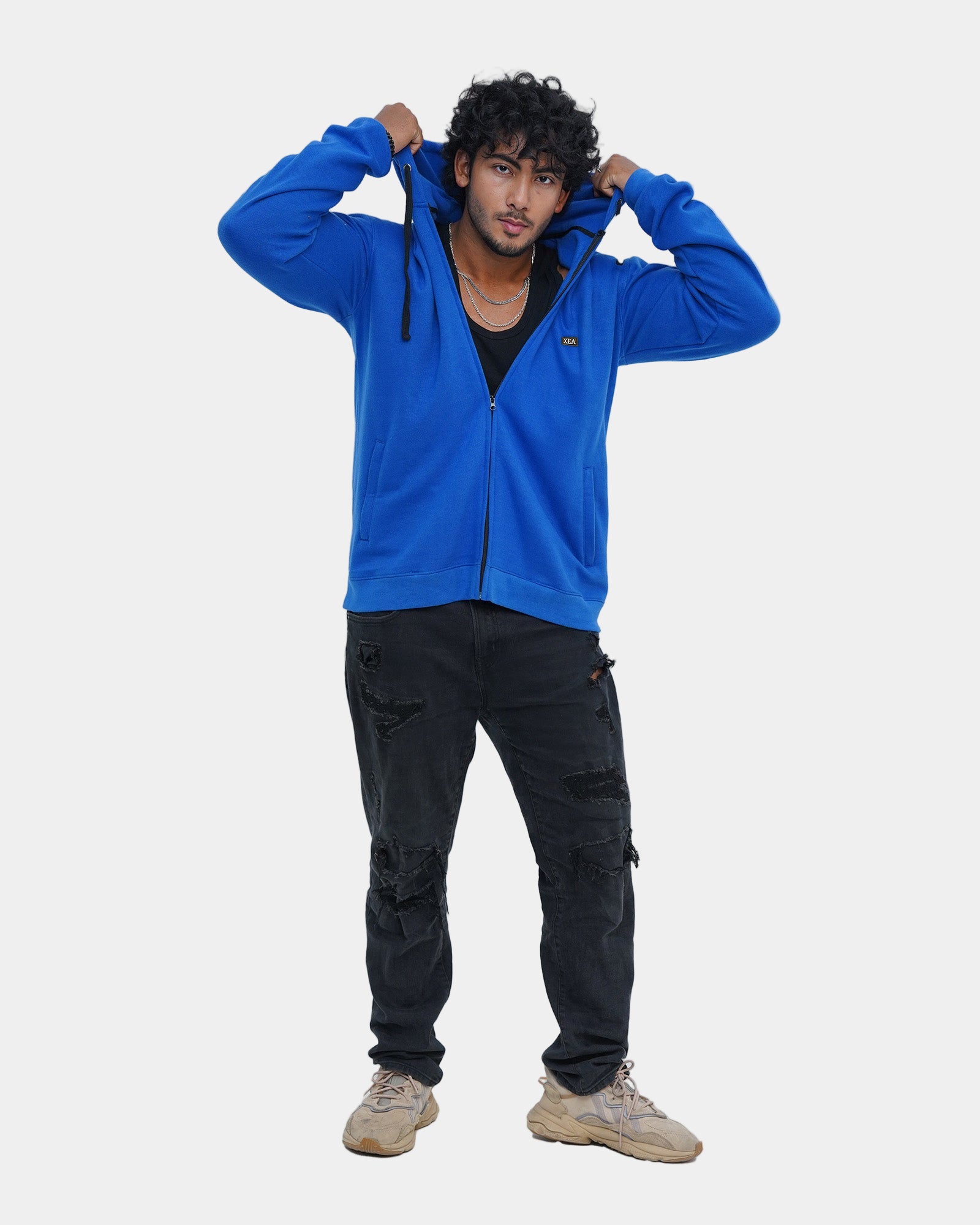 Person wearing a blue zipper hoodie and black pants on a light gray background