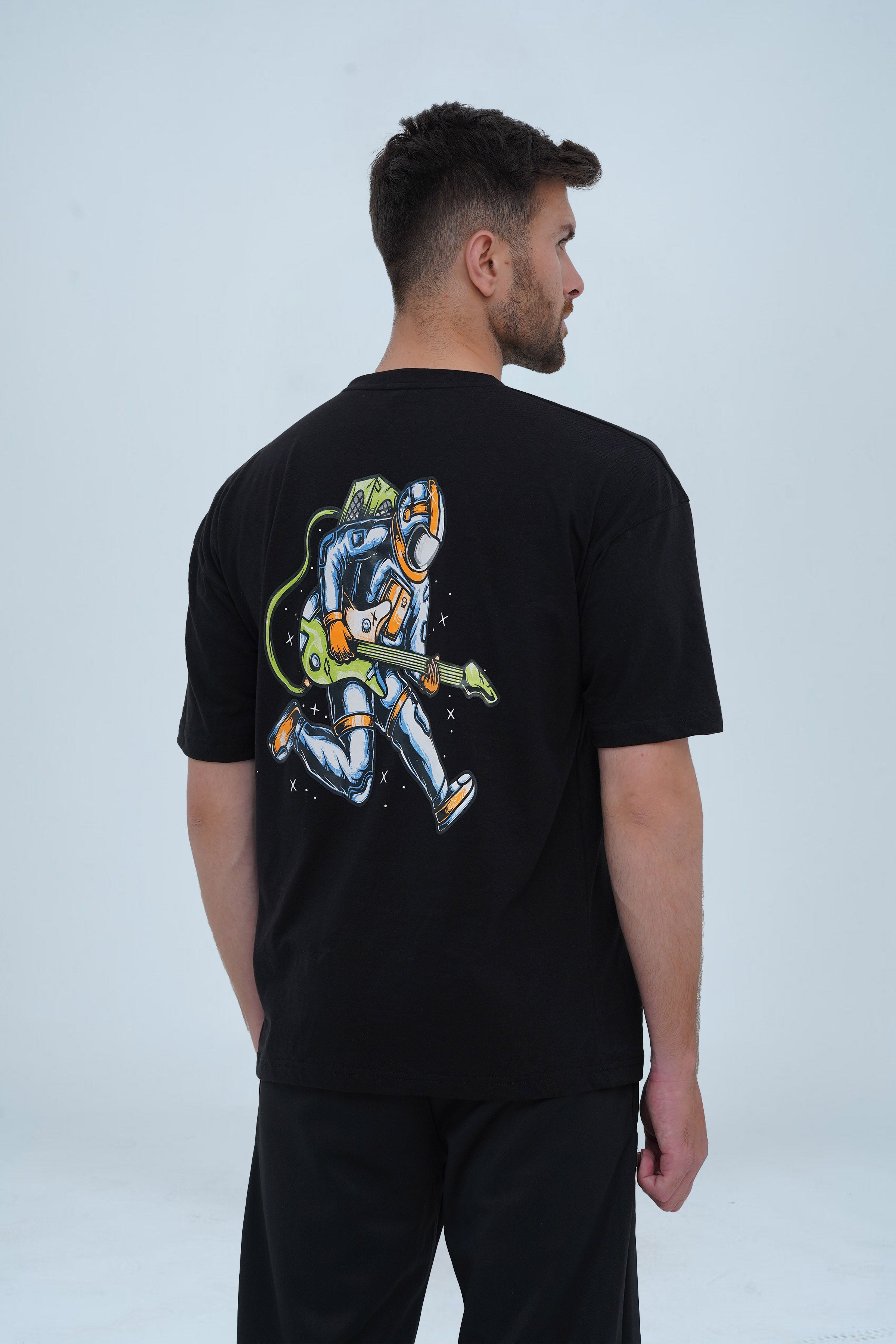 A trendy black drop-shoulder T-shirt showcasing a detailed graphic of an astronaut playing a guitar in space, adding a cosmic edge to urban fashion