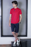 A person wearing a red crew neck t-shirt and black shorts, standing in a room with mirrored doors.