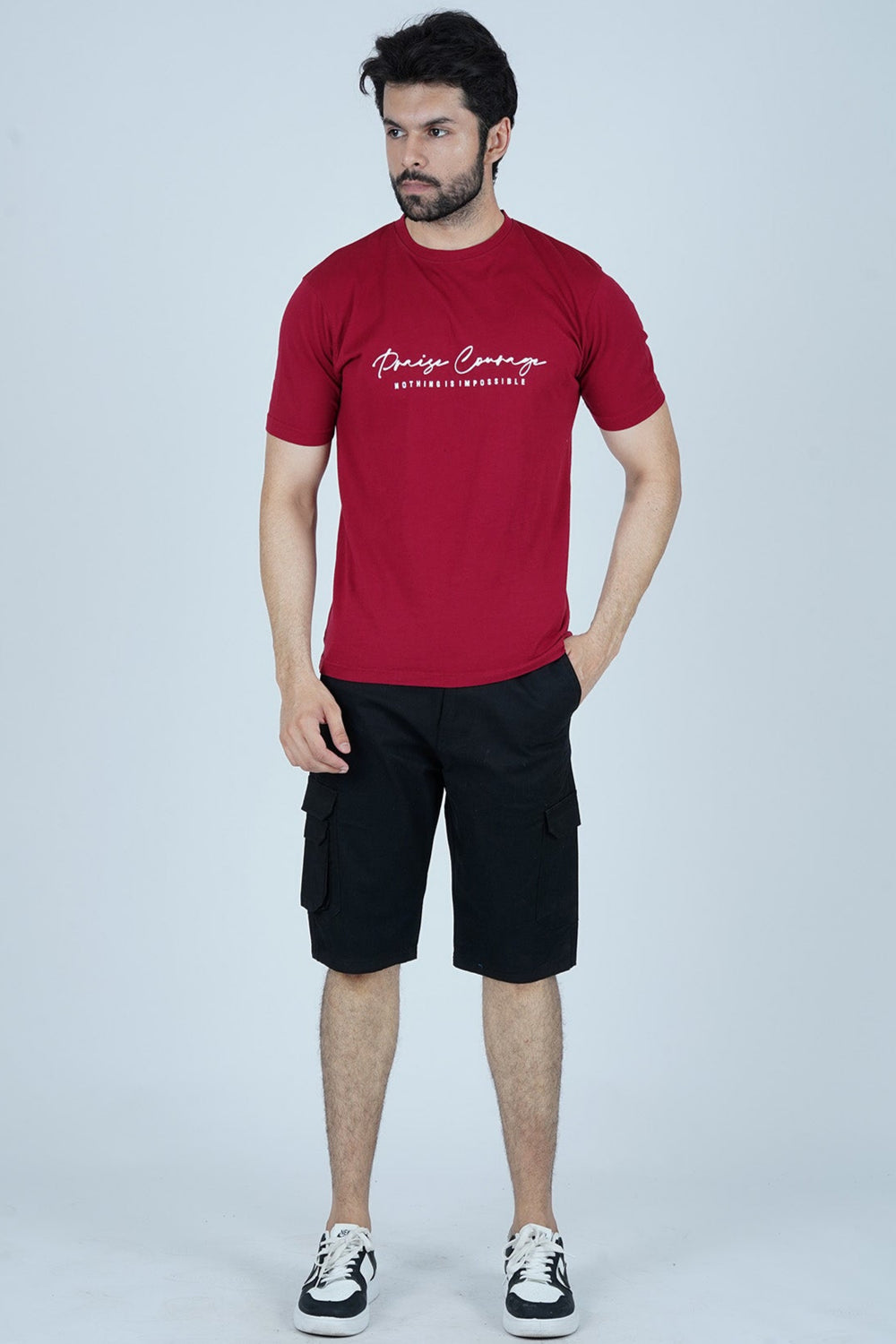 A man wearing a red t-shirt with the text 'Praise Courage' standing against a plain background.