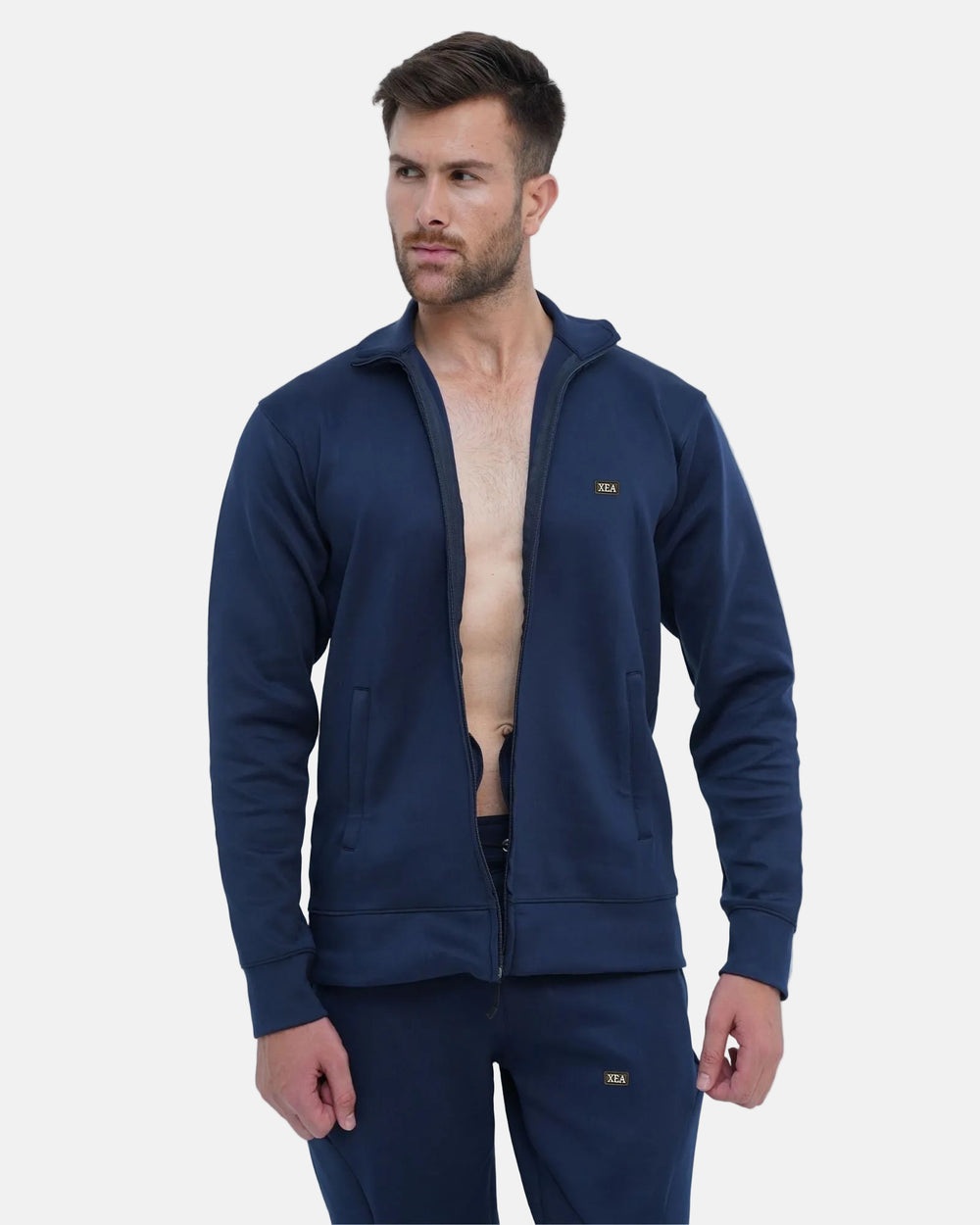 Man wearing a navy blue tracksuit with a brand logo on a light gray background