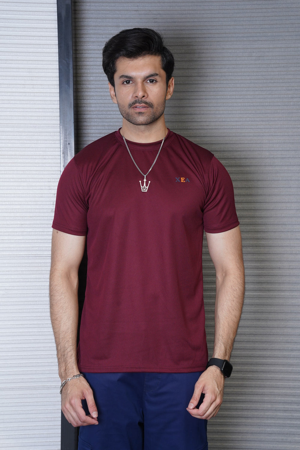 Man wearing a maroon t-shirt with a brand logo against a metallic shutter background