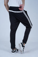 A man wearing black trouser/pants with white stripes on the side, a white t-shirt, and white sneakers. The image shows the pants in a vertical orientation.