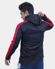 Person wearing a black and red tracksuit with a hood on a light gray background