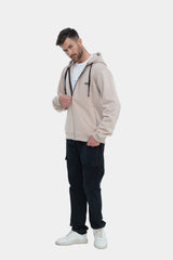 Man wearing a beige hoodie, black pants, and white sneakers on a white background