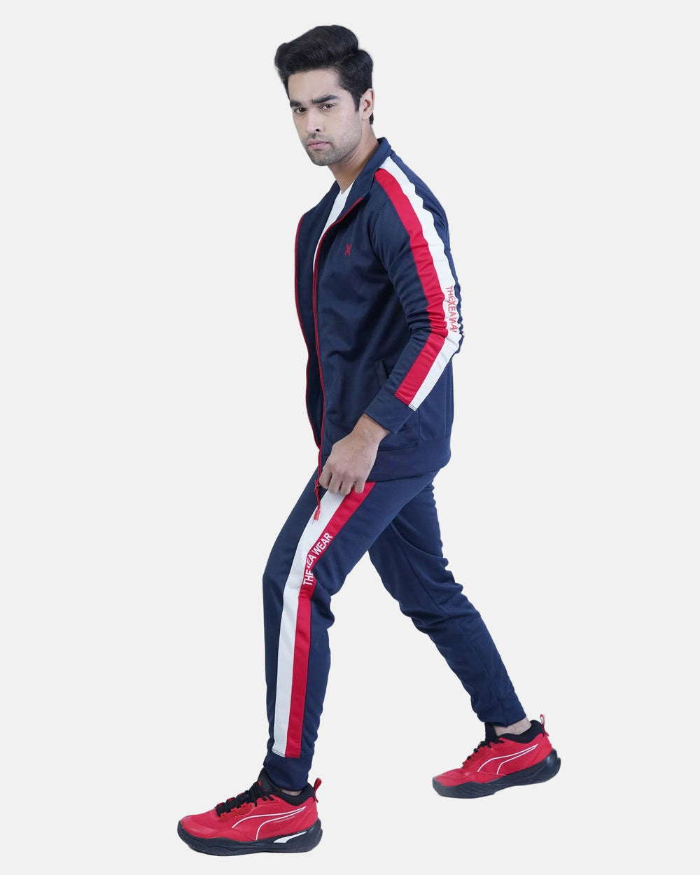 Man wearing a navy tracksuit with red and white stripes on a light blue background